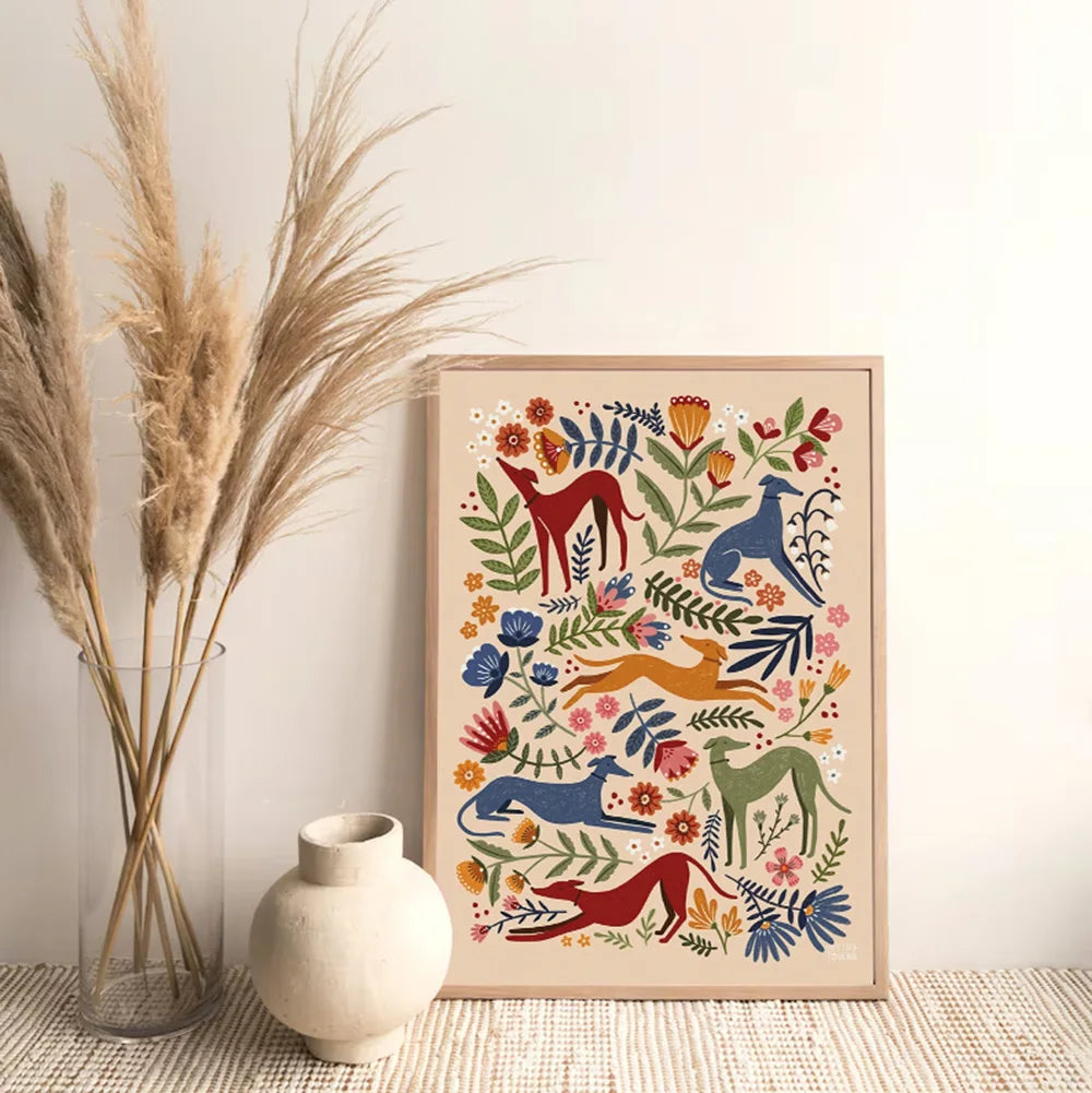 Framed artwork with colorful animals and flowers next to a vase and dried plants on a textured surface.
