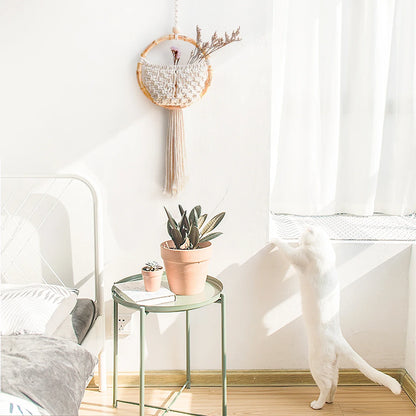 Small round glass table with a potted plant and decorative items in a room with a white wall and a cat sitting on the floor.